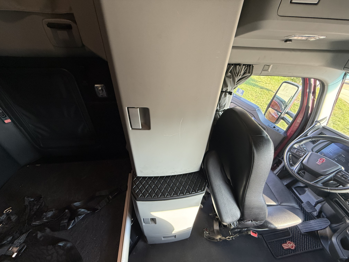 Kenworth T680 cab interior showing driver seat and overhead console with a vertical cabinet and storage area.