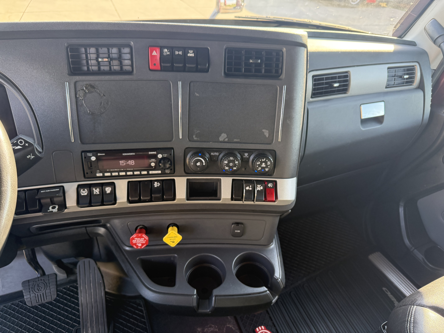 Kenworth T680 truck interior dashboard view showing center console with controls, vents, and cup holders.