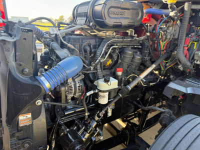Kenworth T680 engine bay view showing air intake, hoses, belts, coolant reservoir, and various engine components.