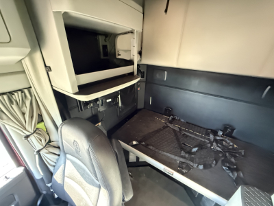Kenworth T680 sleeper cab interior showing bunk area and storage shelf with harnesses and seating in front.
