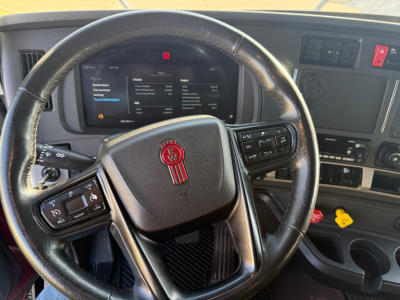 Interior of a Kenworth T680 steering wheel and dashboard with digital infotainment screen and control stalks visible.