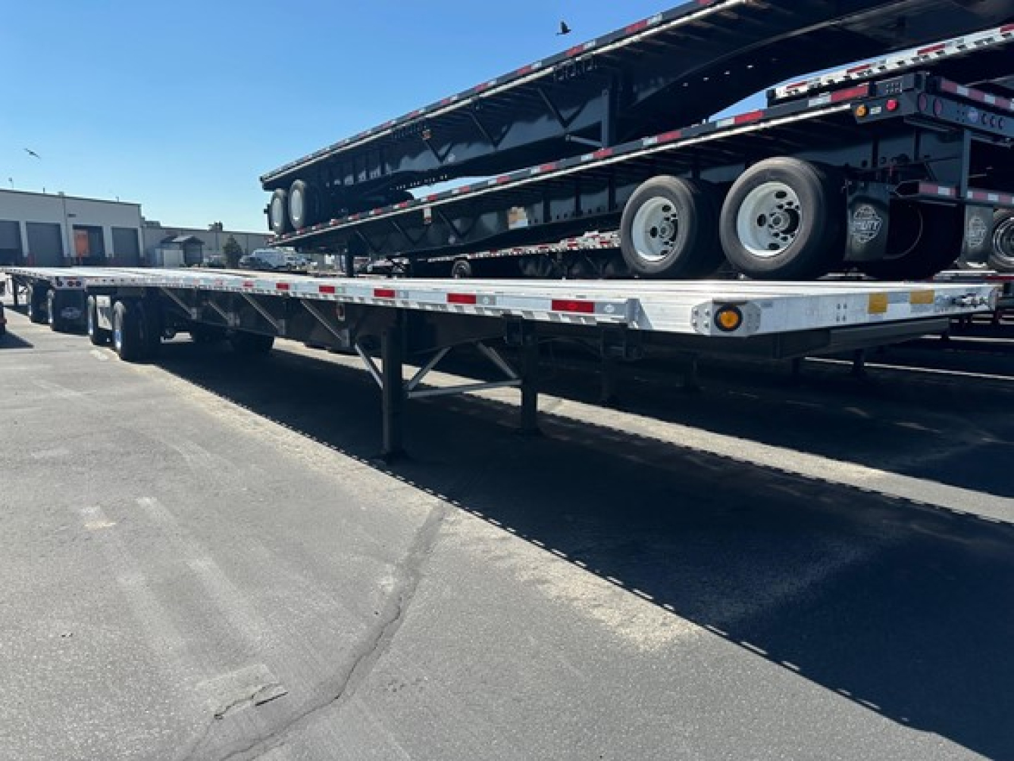 Flatbed trailer with stacked deck and dual rear axles visible; long trailer frame and undercarriage details, loading area showing reflective tape and support beams.