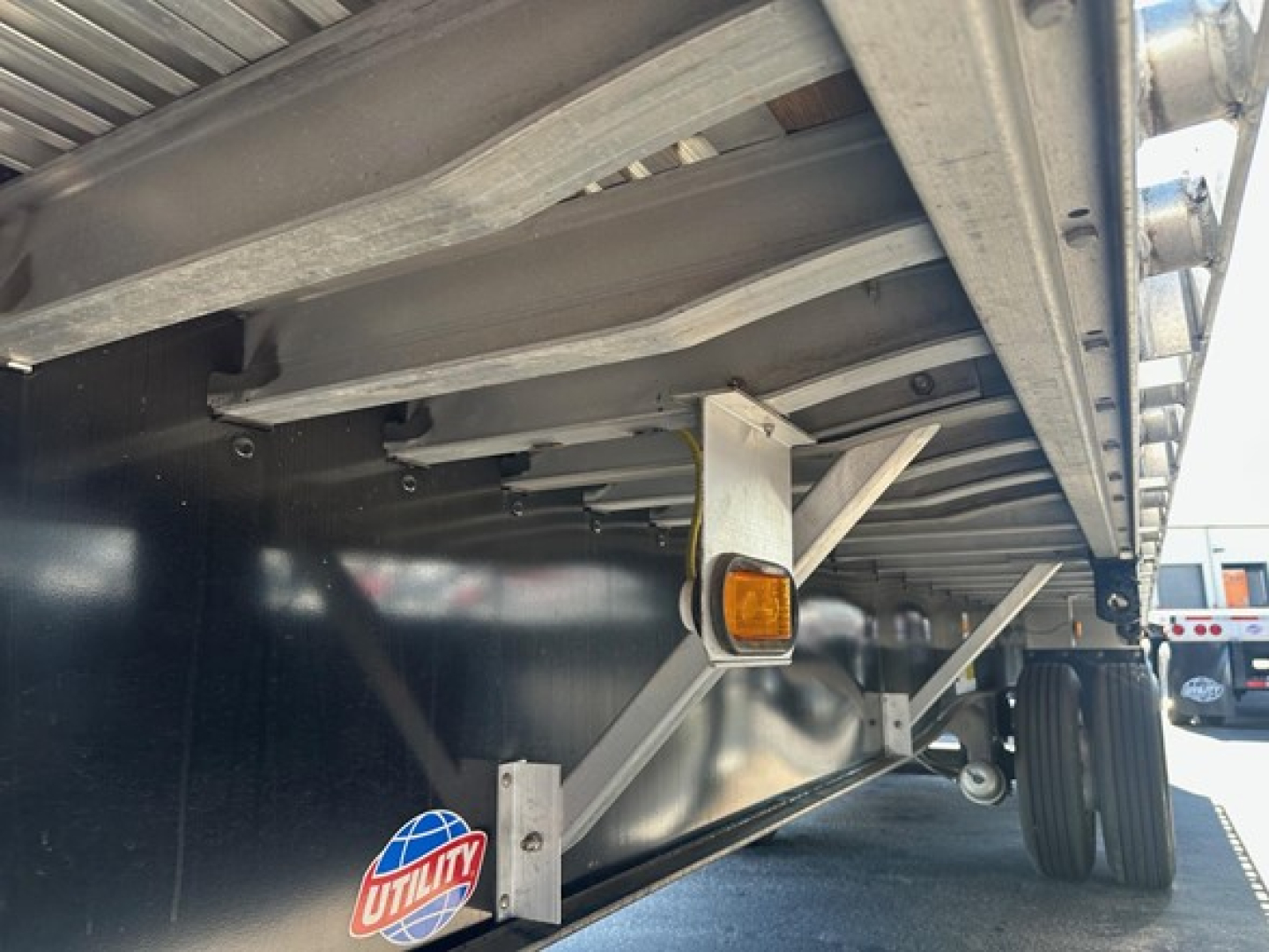 Utility spread air combo flatbed trailer side undercarriage showing frame, suspension, and wheel; orange side marker light visible.