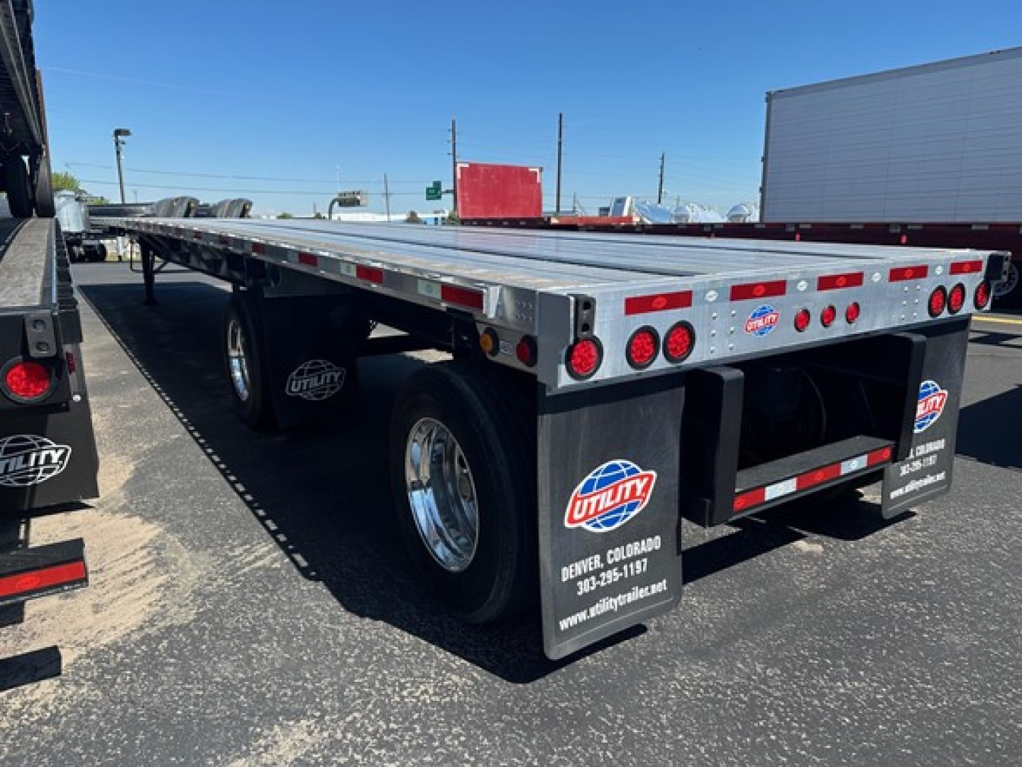 Trailer rear and side view of a 2024 Utility Spread Air Combo Flatbed with dual rear axles, reflective striping, and Utility branding mud flaps.