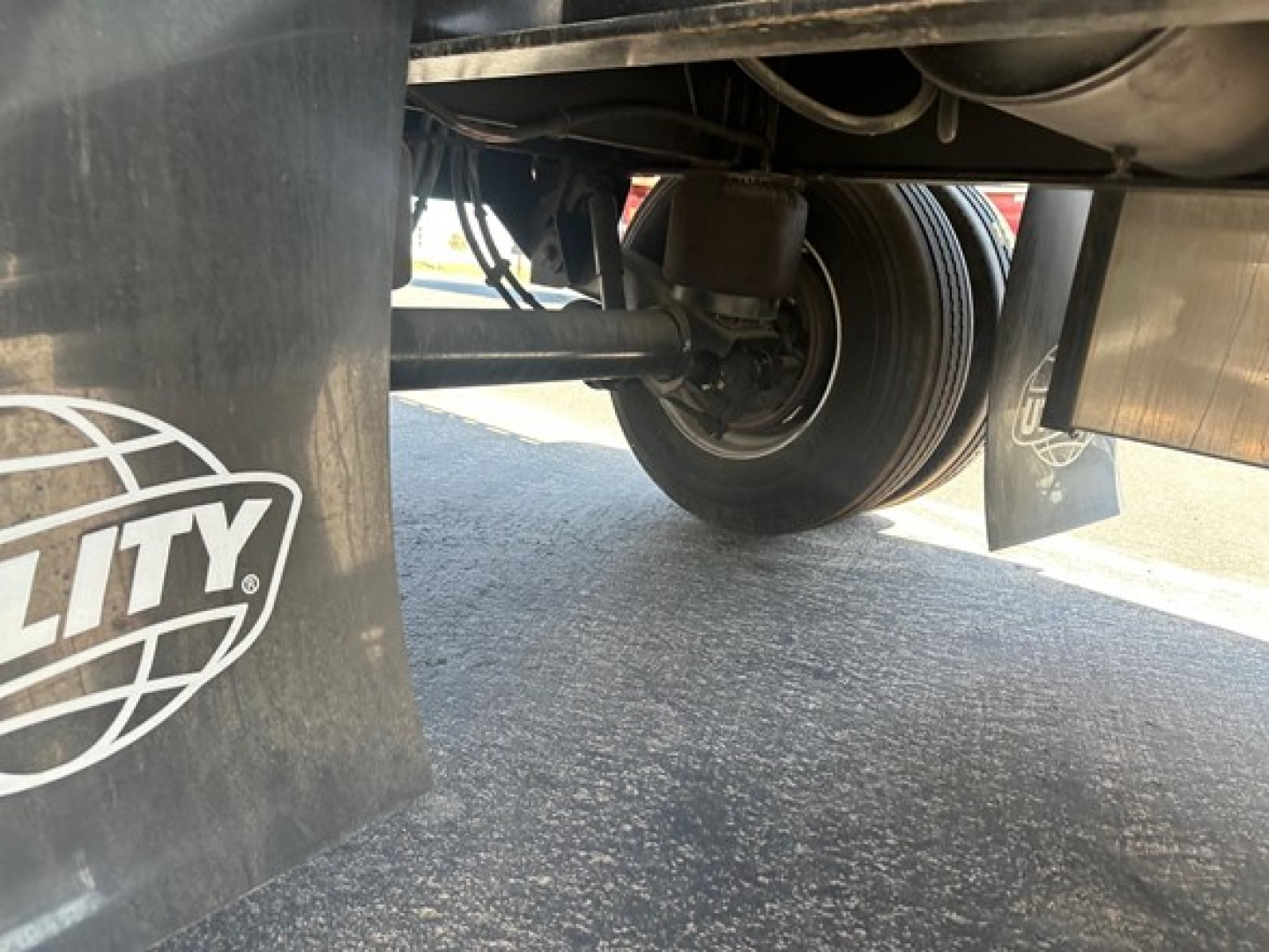 Trailer undercarriage showing axles, leaf springs, and tire with utility logo mudflap visible.