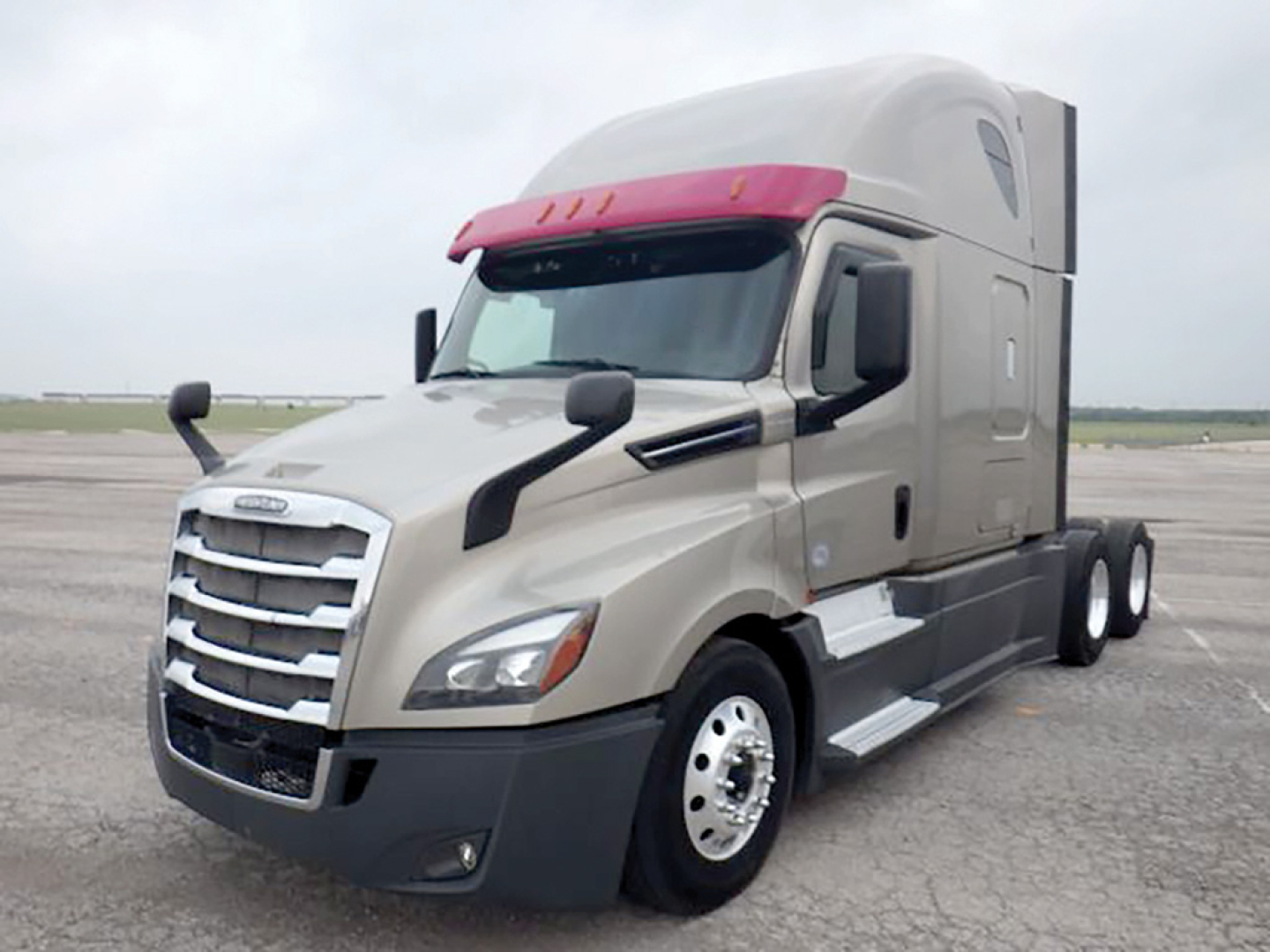 Freightliner Cascadia126 truck in beige with red sun visor, view of cab and front wheel from passenger side.