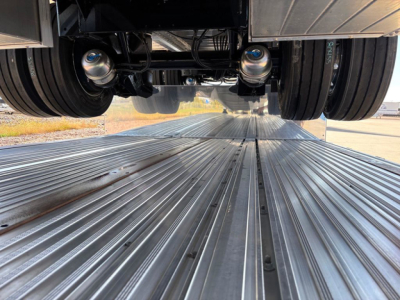 Dropdeck trailer underside with twin axles and metal deck planks, view from between the wheels looking forward
