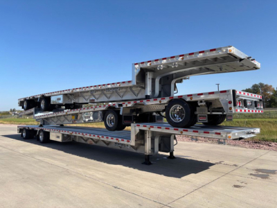 Dropdeck trailer stacked on a lowboy with multiple deck sections, aluminum frame, and dual rear axles, elevated section showing hydraulic mechanism.