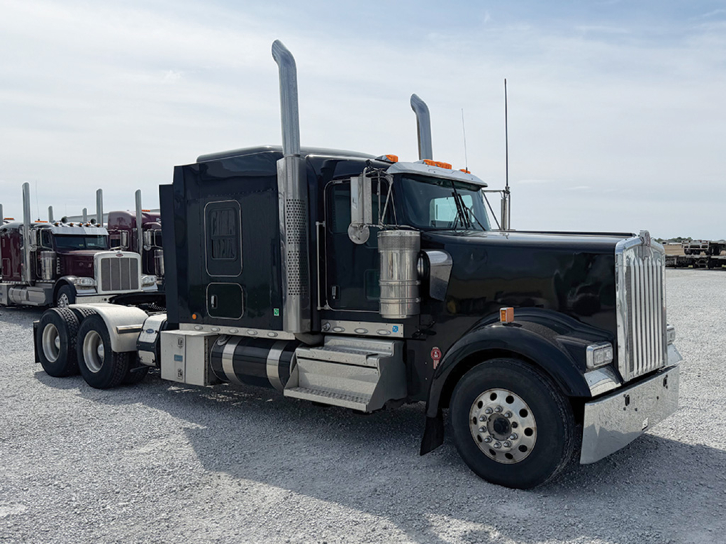 Kenworth W-900L AeroCab tractor truck in service view showing black cab, tall exhaust stacks, chrome front bumper, and dual rear axles with fifth wheel.