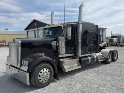 Kenworth W900L AeroCab tractor from left-front angle showing large chrome grille, dual exhaust stacks, black sleeper cab, and dual rear axles.