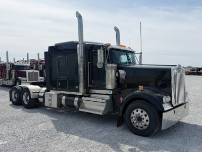 Kenworth W-900L AeroCab tractor truck in service view showing black cab, tall exhaust stacks, chrome front bumper, and dual rear axles with fifth wheel.