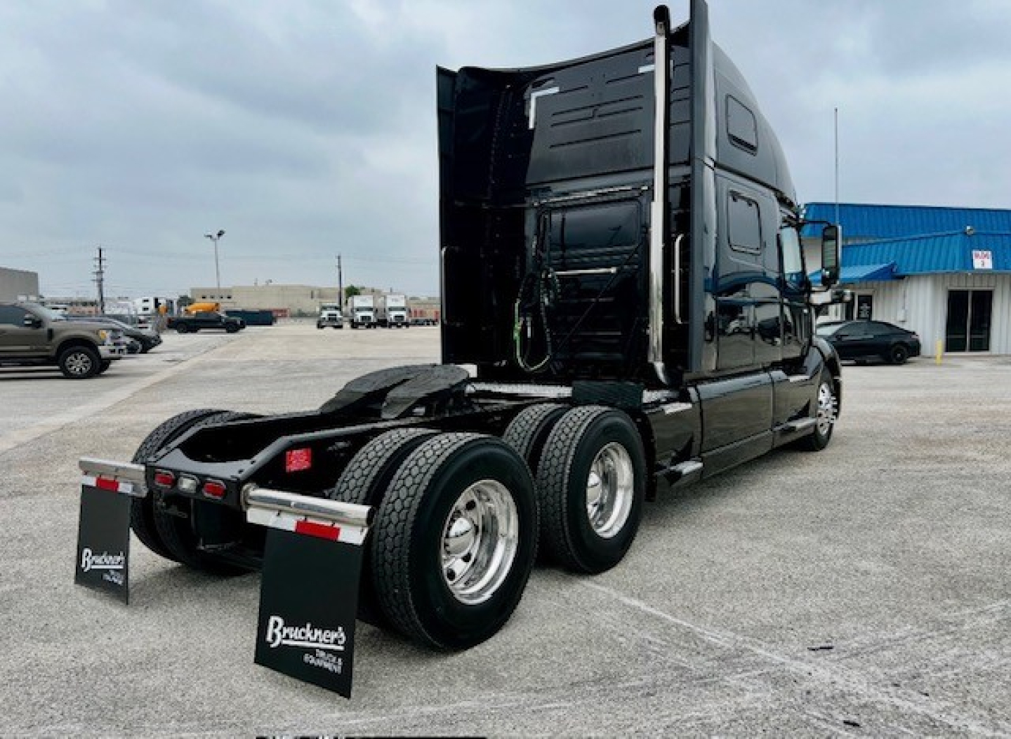 Truck rear view showing sleeper cab, dual rear axles, mud flaps, and fifth wheel on a black Volvo VNL860 tractor.