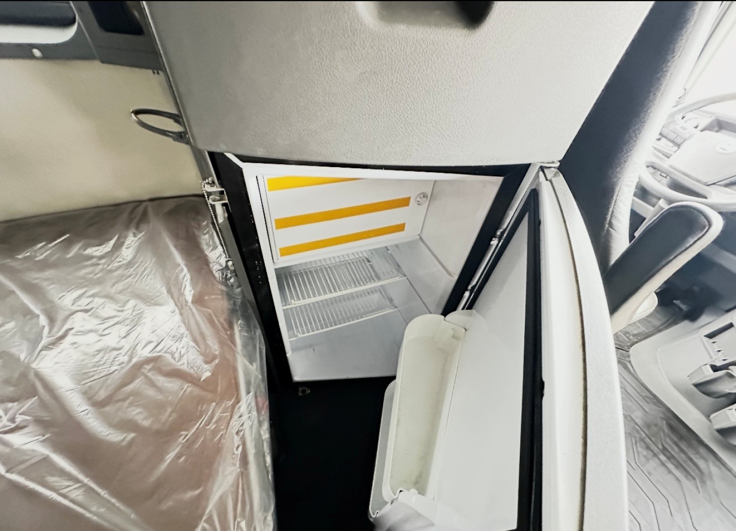 Volvo VNL860 sleeper truck interior showing open small refrigerator compartment with empty shelves and a white door.