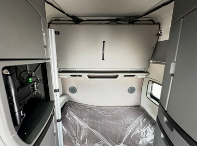 Volvo VNL860 sleeper cab interior showing cargo area with side walls and overhead bunk area, partial left control panel, protective plastic on floor.