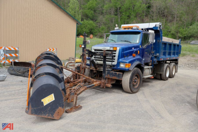 Medium-duty dump truck with winter plow attachment in view, blue cab, orange safety mirrors, Sterling LT9500 series insignia, multiple wheels, plow blades labeled with TI-?