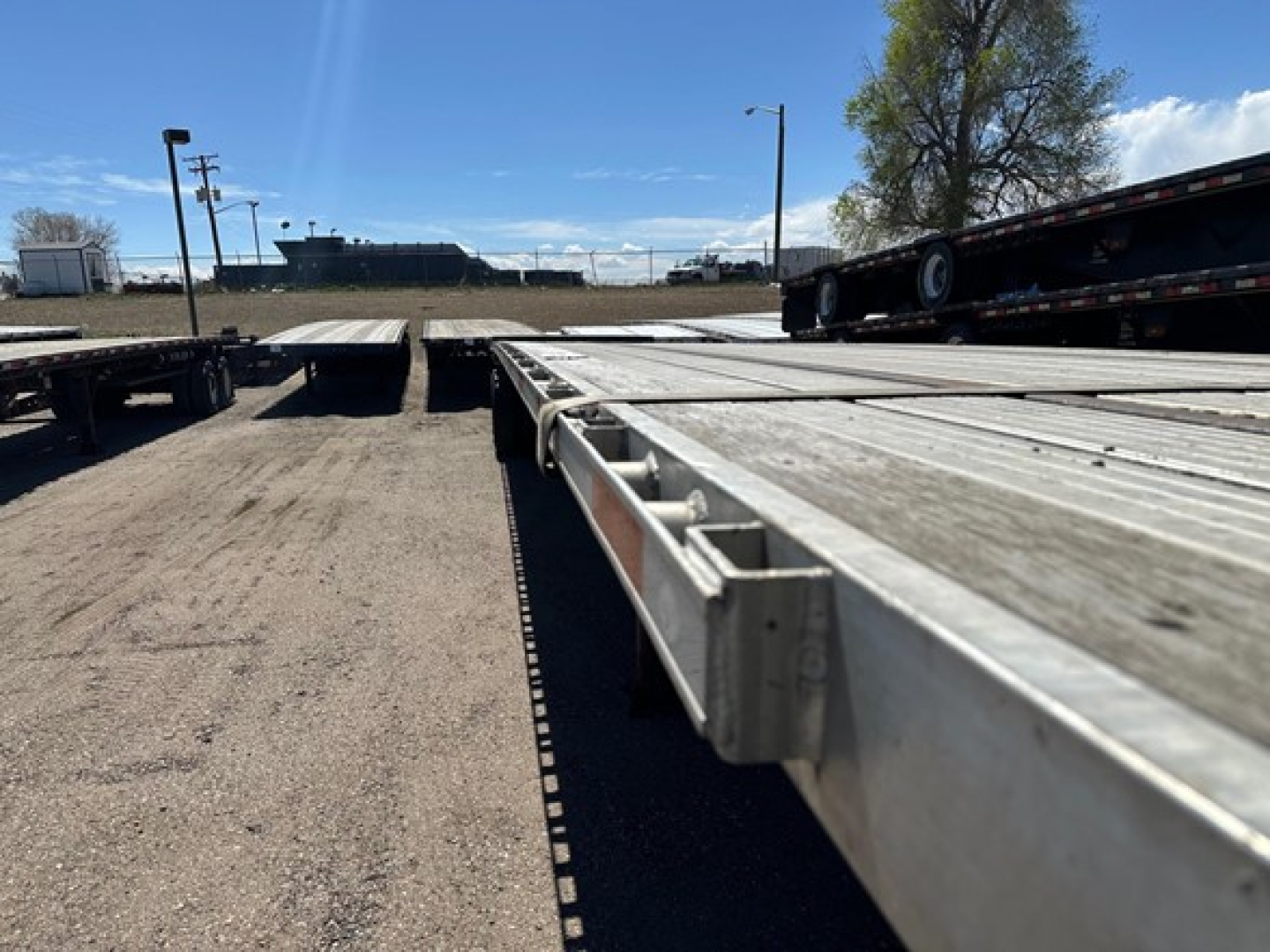 Flatbed trailers with long aluminum deck and tandem axles, utility trailer market sign in distance, clear sky