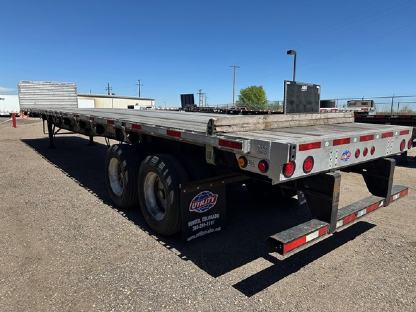 Utility 4000Ae flatbed trailer showing dual rear axles and aluminum flat deck with reflective tape and rear bumper; visible sign near wheels reads Utility "Vehicle" and phone number; gravel lot.