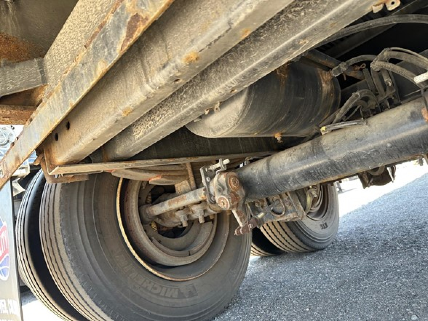 Trailer undercarriage showing dual axles, leaf springs, and rubber tires of a Utility 4000Ae flatbed trailer.
