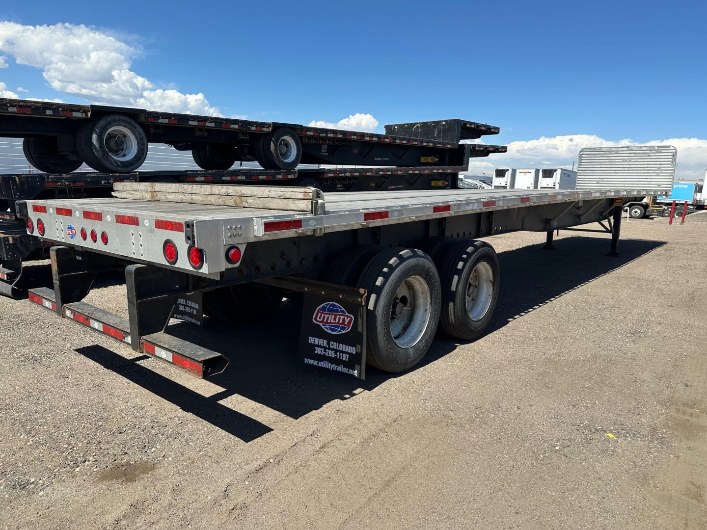 Flatbed trailer with dual rear axles and lowboy deck, Utility brand marker, showing aluminum siding and tail lights; stacks of equipment on bed.