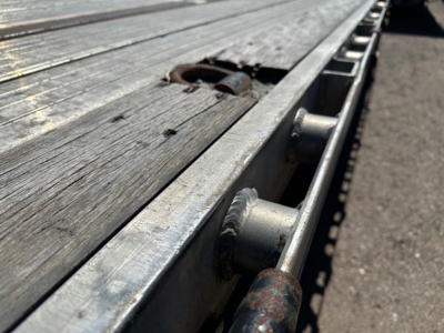 Flatbed trailer deck from a 2020 Utility 4000Ae showing wooden planks, metal edge, and side rail with stake pockets.