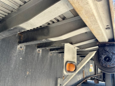 Trailer underside showing metal beams and a spindle; orange-handled jack or adjustment knob visible on a vertical bracket.