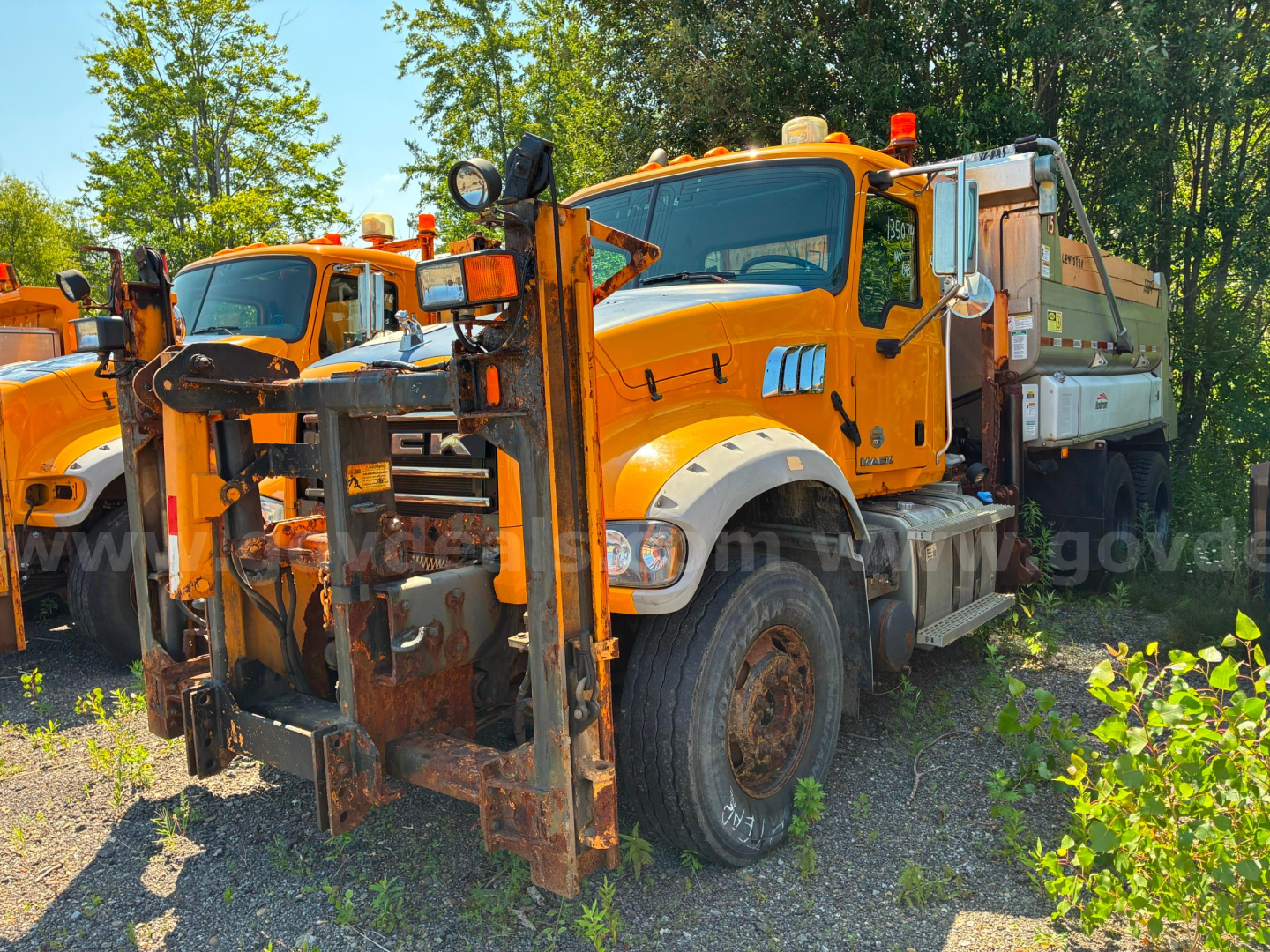 Mack GU713 dump truck in-service showing front struck forklift-like attachment and orange cab with white fenders.