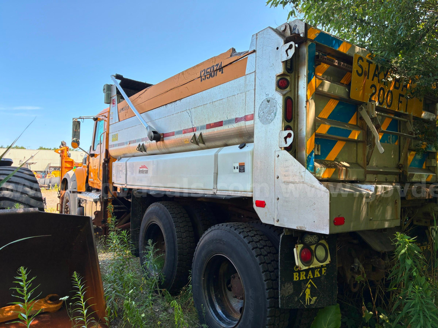Mack GU713 dump truck rear and side view with orange cab and silver dump body, showing decals and brake light cluster.