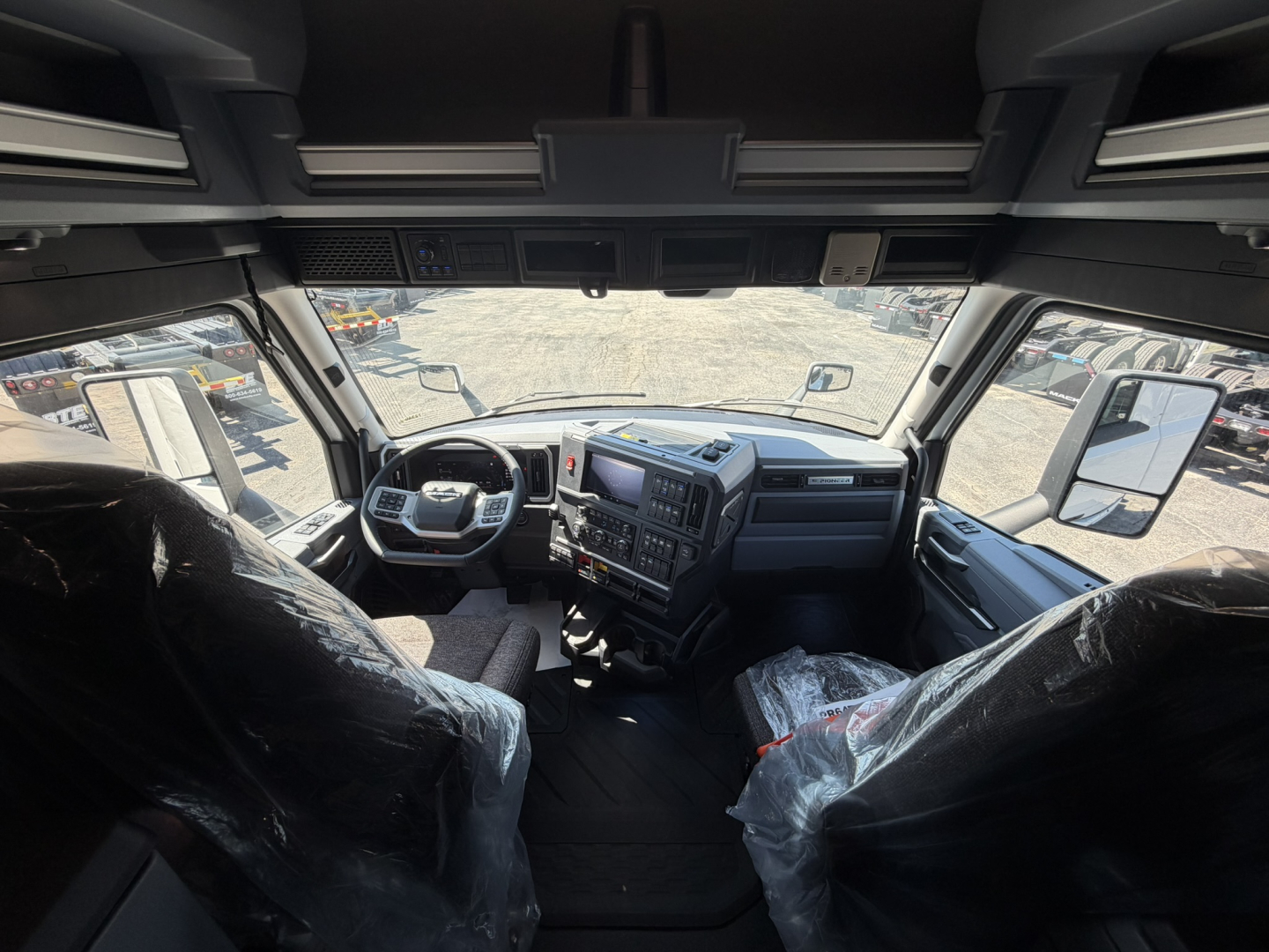 Truck cab interior view showing steering wheel, dashboard, and front seats in a Mack PR64T76H sleeper cab.