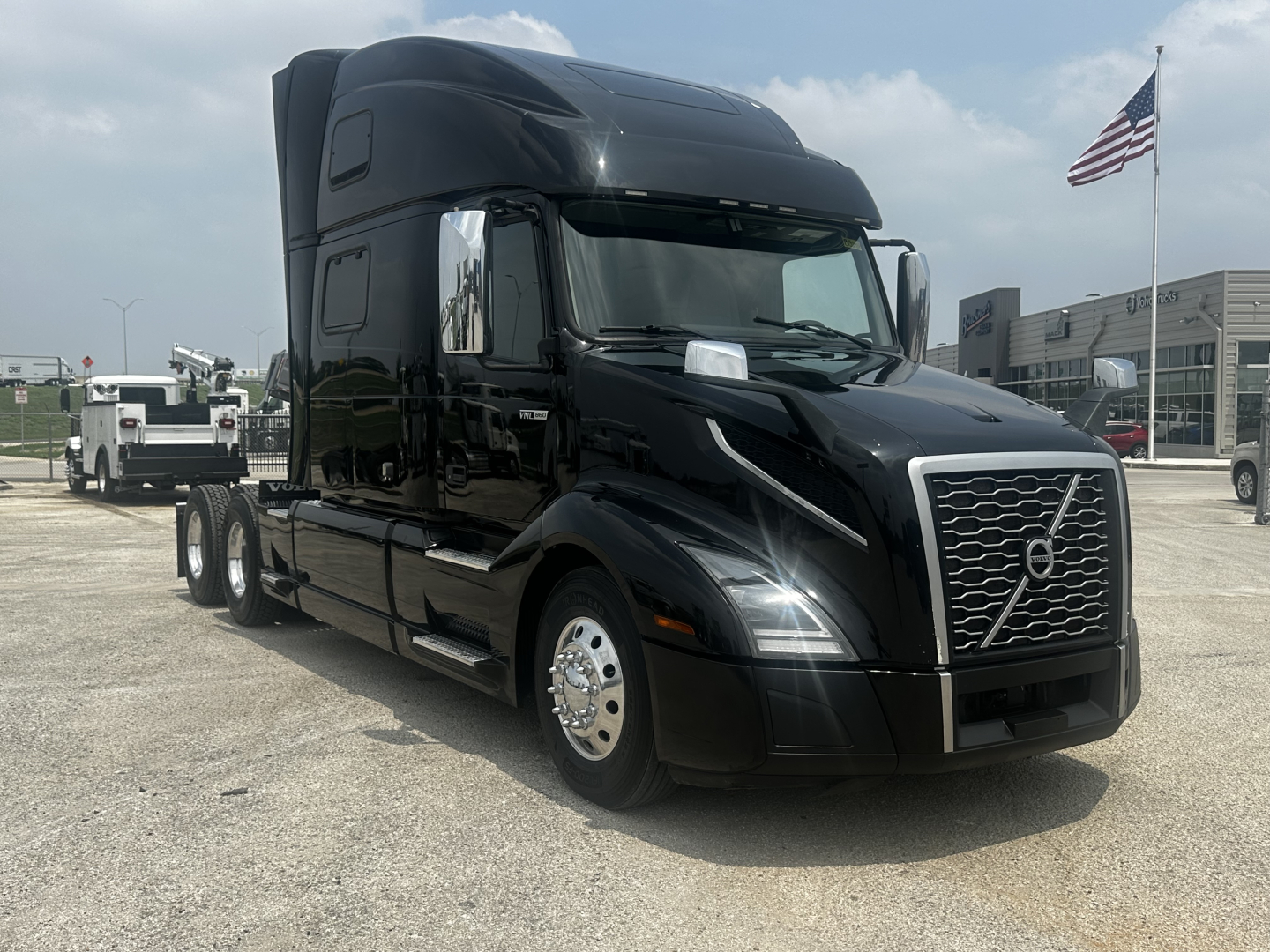 Black Volvo VNL860 semi-truck in a lot, front-left angle, chrome grille with Volvo emblem, large sleeper cab, American flag in background.