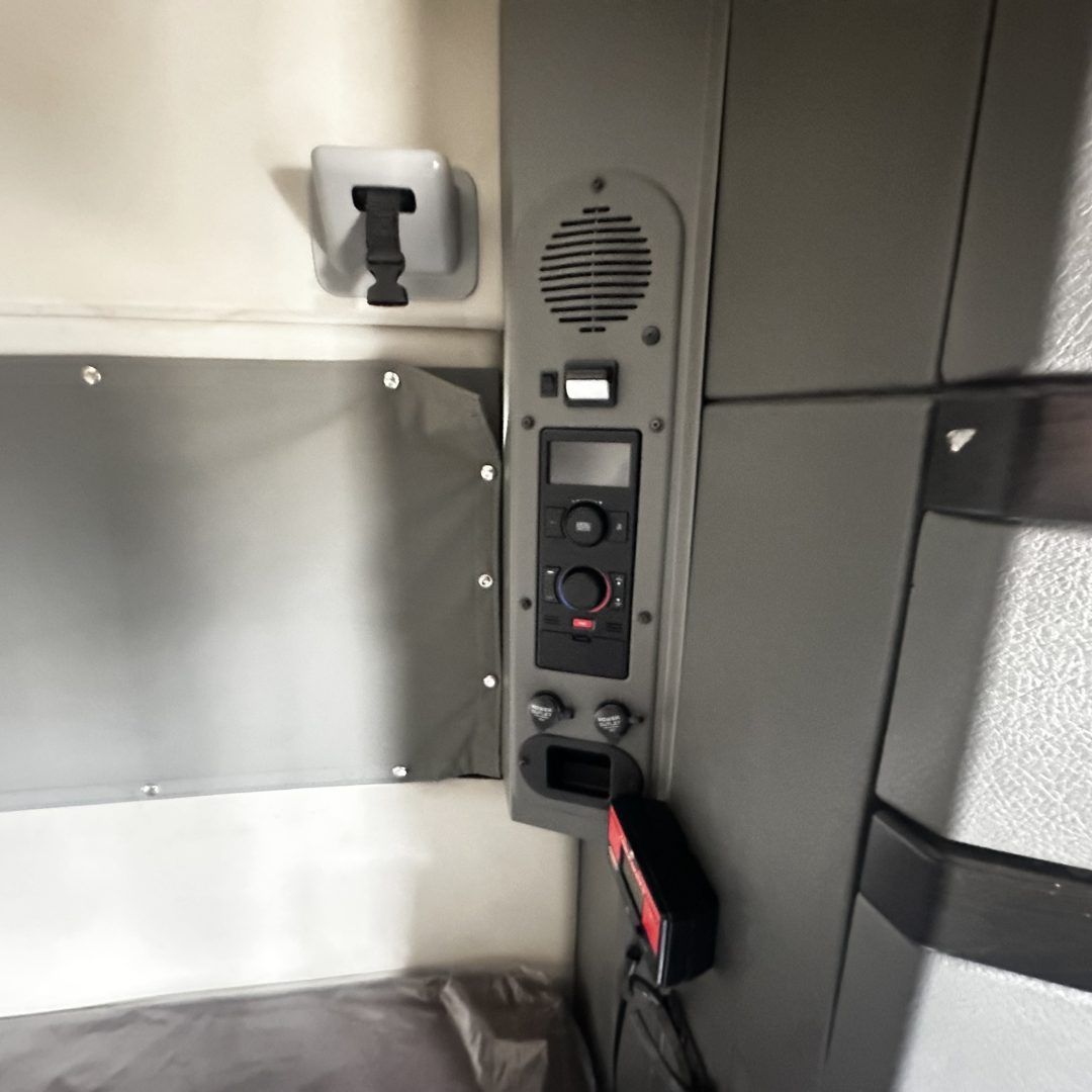 Cab interior panel of a Volvo VNL860 sleeper showing control switches and a speaker grill. Visible text: small digital display and circular dials; no legible model text.