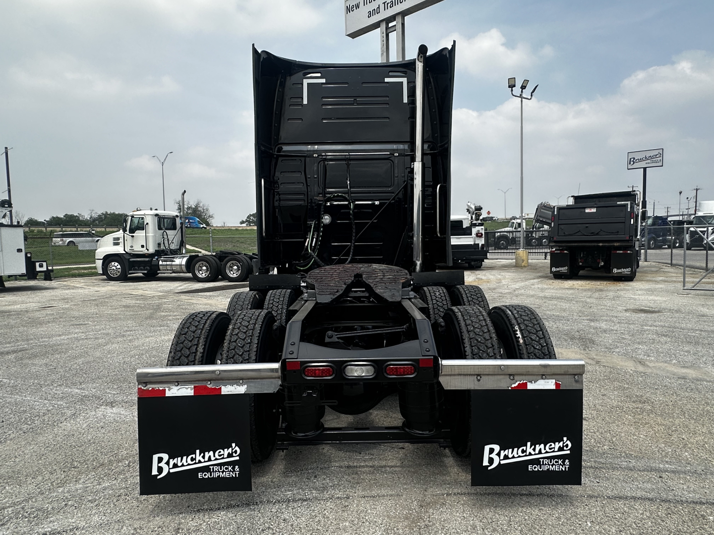 Truck rear view showing two mud flaps with ‘Buckner’s Trucks & Equipment’ logos, chassis, dual rear axles, and fifth wheel visible.