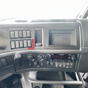 Dashboard of a Volvo truck showing control switches, air vents, and a Volvo stereo. Visible labels include engine controls, option switches, and a red hazard switch.