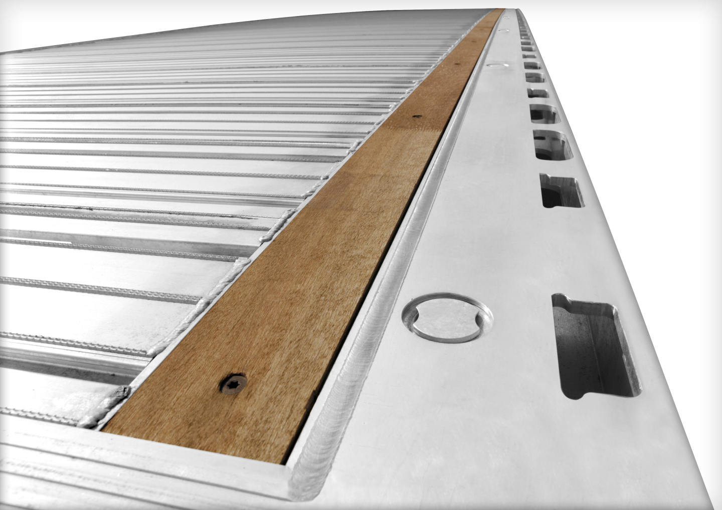 Flatbed trailer corner showing aluminum deck with wood crosspiece and tiedown rings, side cutouts, and reflective edge