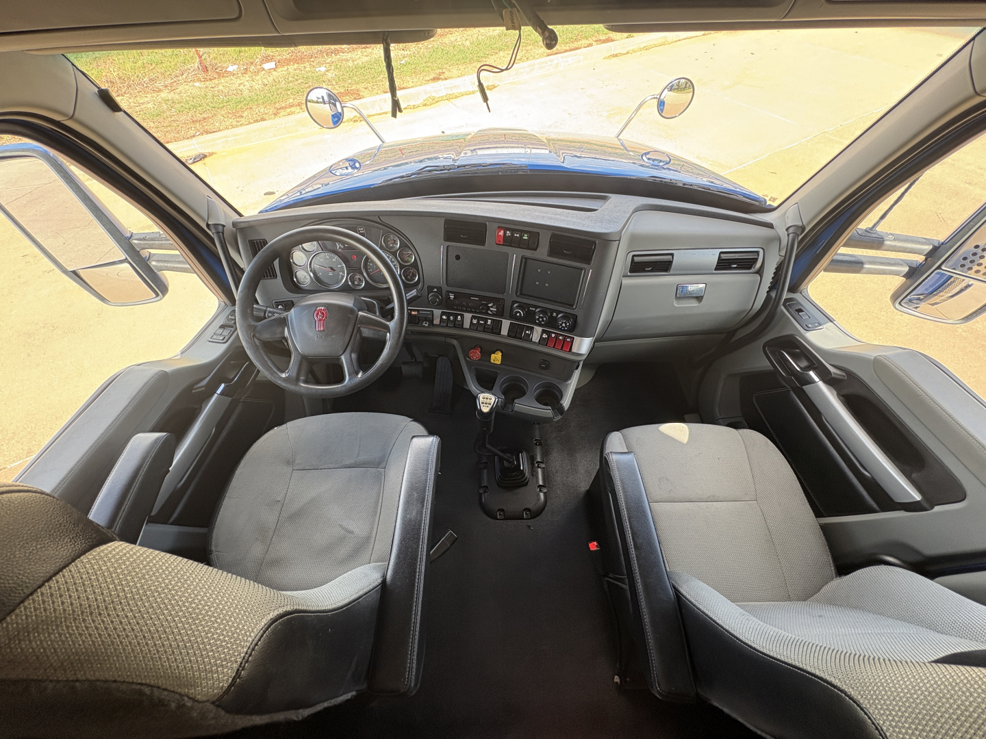 Kenworth T880 cab interior view showing steering wheel, dashboard, and two front seats in a sleeper truck. Visible gauges, control panel, and center console.