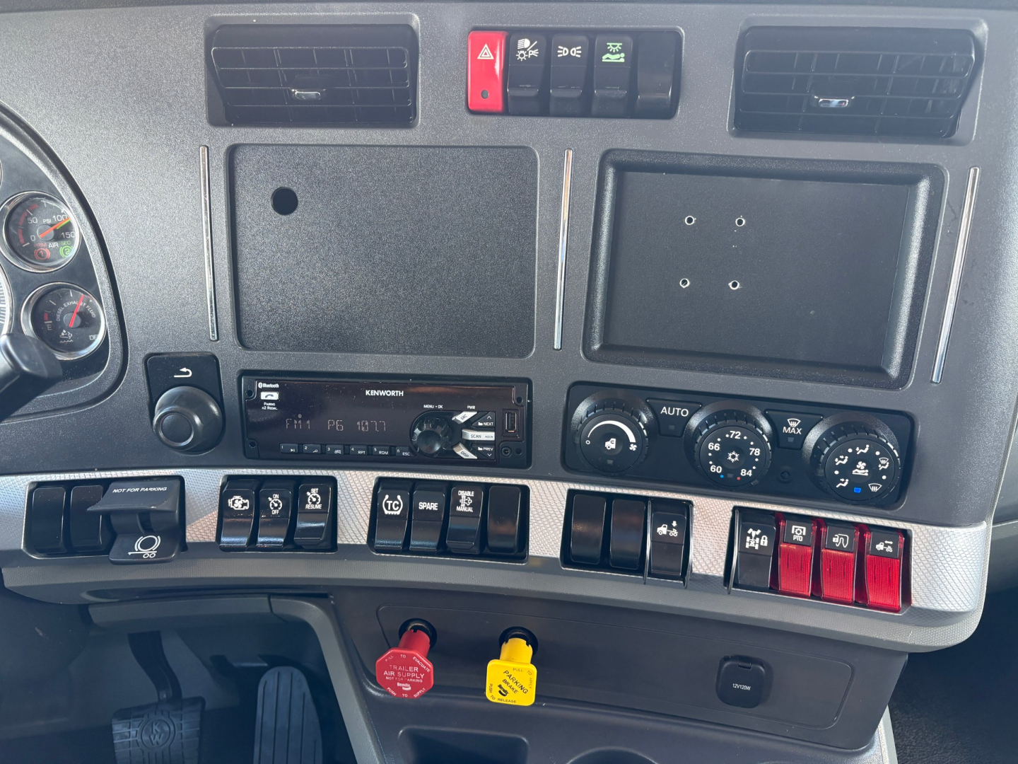 Kenworth T880 dashboard cluster and center panel showing various switches and controls, with radio and climate dials, red and yellow key locks visible.
