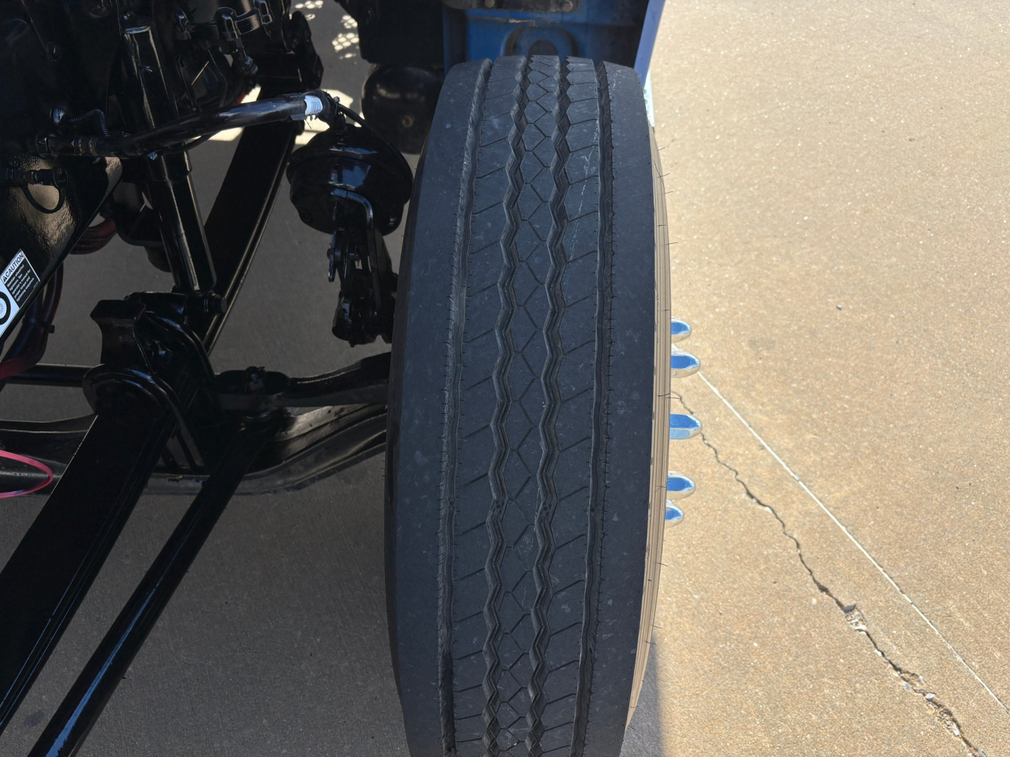 Tire mounted on Kenworth truck showing tread pattern and suspension components in wheel well.