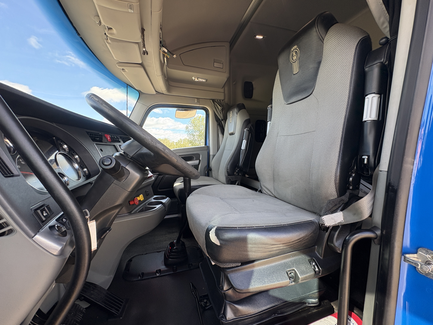 Cab interior of a 2020 Kenworth T880 showing driver's seat and steering wheel with grey upholstery and a glimpse of the dashboard