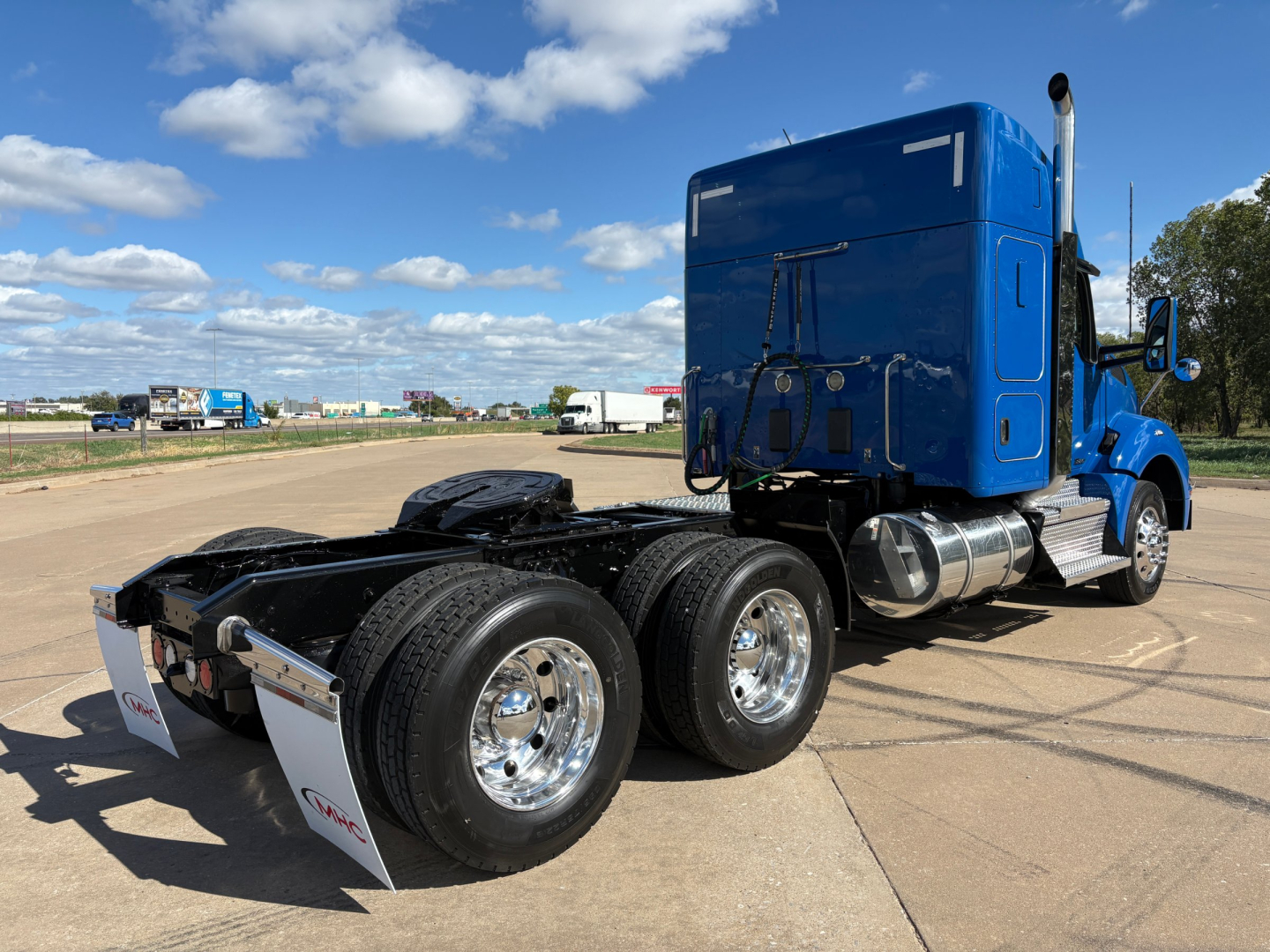 Kenworth T880 semi tractor in blue, rear view showing dual rear axles and fifth wheel with chrome wheels and mud flaps.