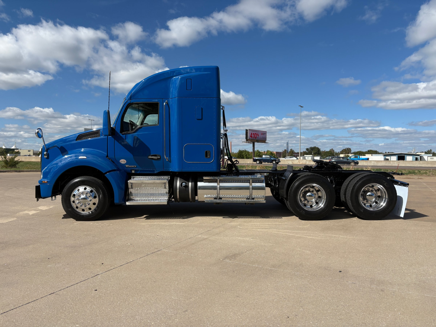 Side view of a blue 2020 Kenworth T880 tractor with sleeper cab, chrome fuel tanks, and dual rear axles in a parking lot.