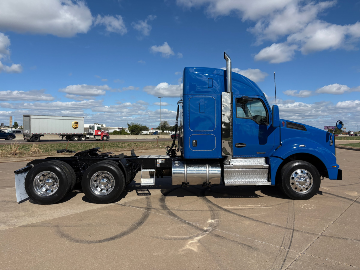 Kenworth T880 day cab tractor in blue, side view showing sleeper cab, chrome fuel tanks, dual rear axles, tires, and exhaust stack.