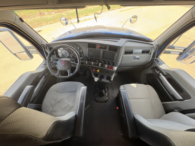 Kenworth T880 cab interior view showing steering wheel, dashboard, and two front seats in a sleeper truck. Visible gauges, control panel, and center console.