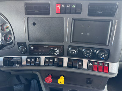 Kenworth T880 dashboard cluster and center panel showing various switches and controls, with radio and climate dials, red and yellow key locks visible.