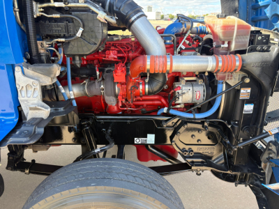 Kenworth T880 engine bay showing red diesel engine, orange intake hoses, blue coolant reservoir, black chassis frame, and various components.