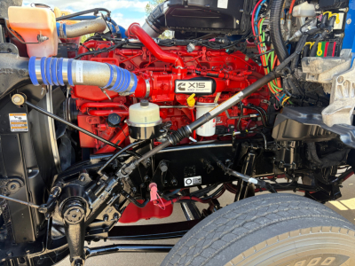 Kenworth T880 engine bay with bright red Cummins X15 label, visible hoses, wiring, and front suspension components.