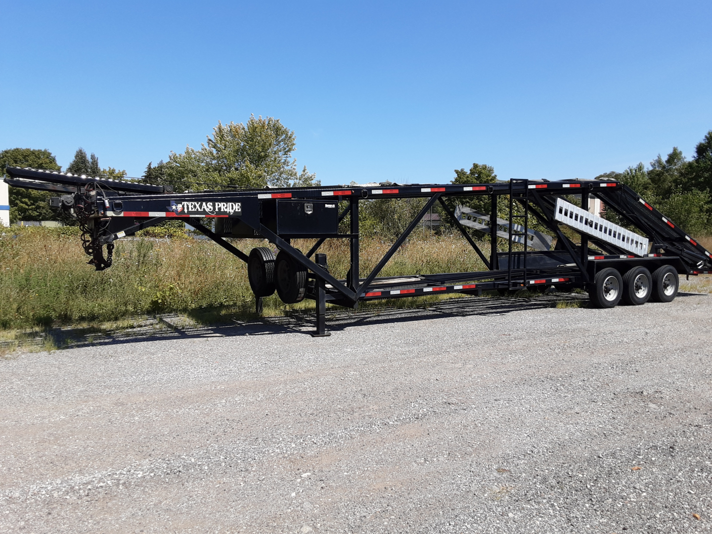 Trailer with 'TEXAS PRIDE' branding showing a long black car carrier with dual rear axles and support frame, side rails, and ramps.
