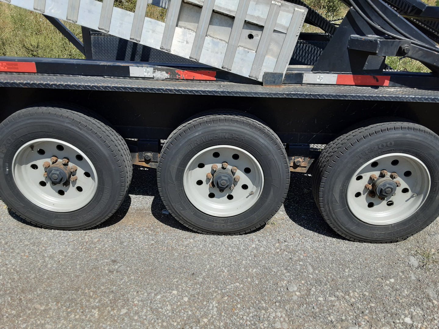 Trailer axle wheels and suspension under a car carrier trailer showing three white rims and black frame.