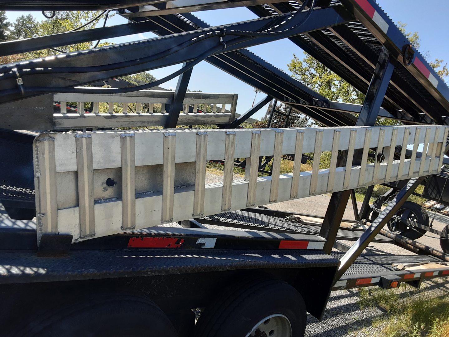 Trailer side view with metal ramp/guard rail on car carrier trailer, blue frame and reflective tape, part of vehicle transport equipment.