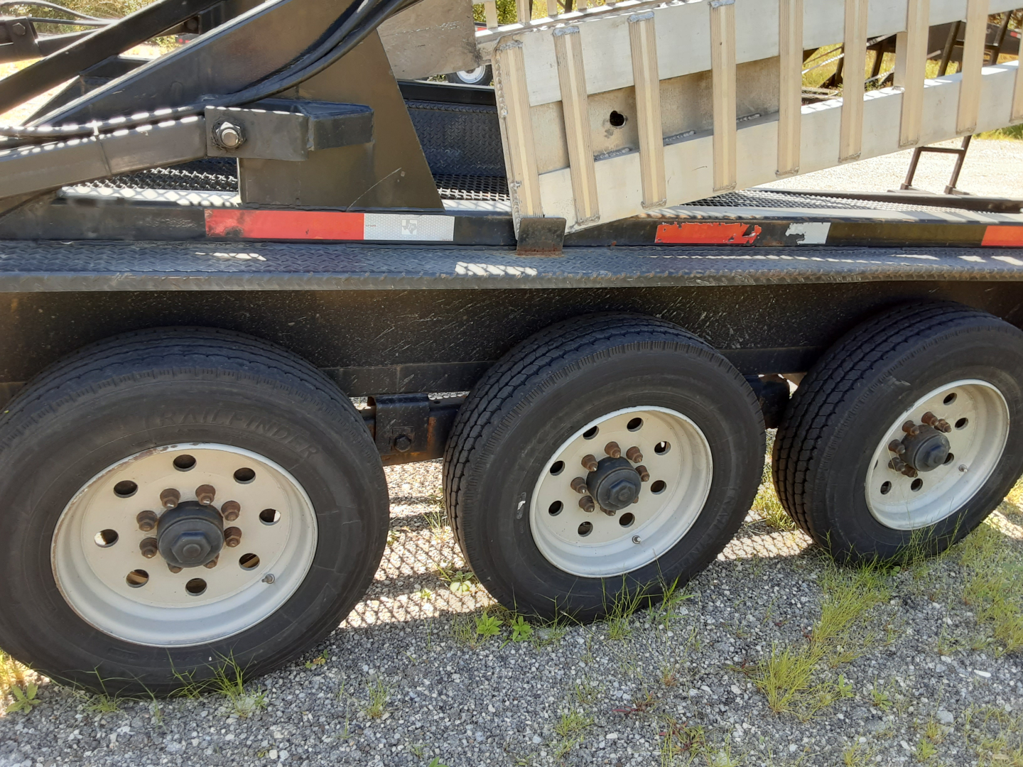 Trailer wheels and side railing of a car carrier trailer showing three axles with white rims and black tires.