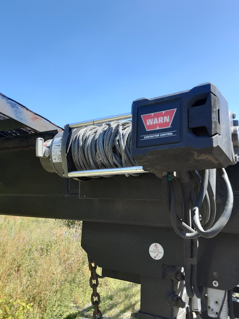 Winch mechanism on a car carrier trailer with coil cable and a WARN winch label visible.