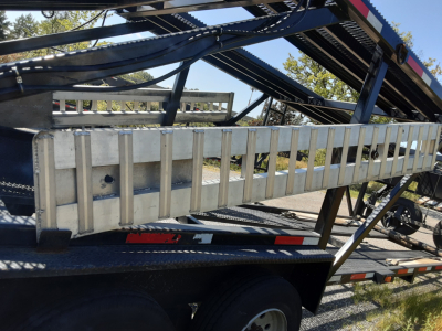 Trailer side view with metal ramp/guard rail on car carrier trailer, blue frame and reflective tape, part of vehicle transport equipment.